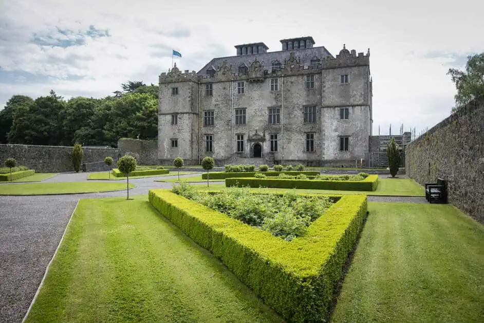Portumna Castle und Gärten, Frontansicht des Schlosses und weite Rasenfläche, auf der sich kleine, durch Hecken eingezäunte Beete befinden