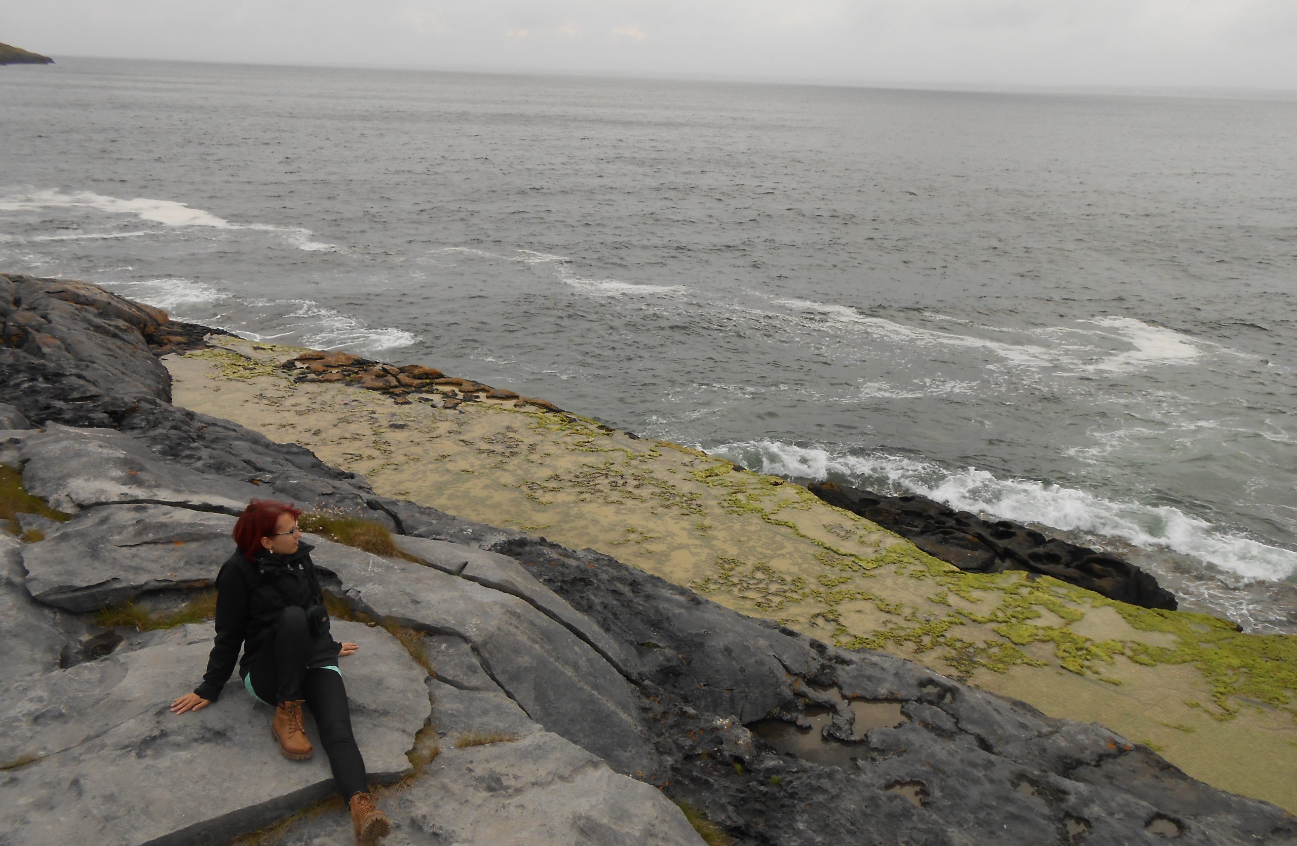 Autorin Jessica Jirschik sitzt auf dem Burren und sieht auf das stürmische graue Meer hinaus