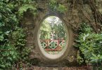 Loch in einer Mauer in den Mount Congreve Gardens, hinter dem man einen Zaun und noch mehr der Gärten sieht