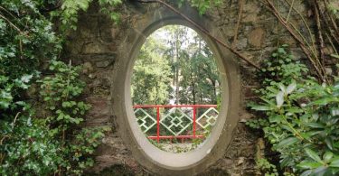 Loch in einer Mauer in den Mount Congreve Gardens, hinter dem man einen Zaun und noch mehr der Gärten sieht